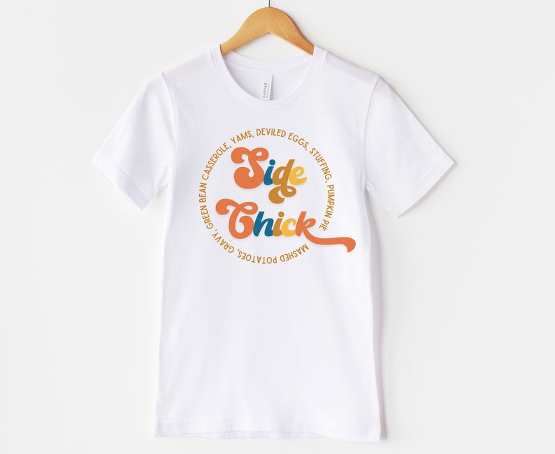 K&ouml;nnte beinhalten: Wei&szlig;es T-Shirt mit einem Grafikdesign, das "Side Chick" in einer Retro-Schriftart sagt. Die Grafik ist von einem Kreis aus Text umgeben, der verschiedene Thanksgiving-Beilagen auflistet.