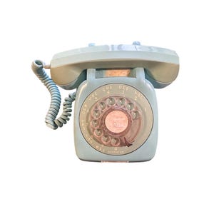 May include: A vintage, light blue rotary dial telephone. The phone has a handset, a dial with numbers and letters, and a coiled cord. The phone is a classic design, likely from the mid-20th century.