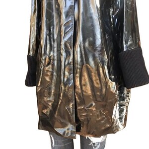 May include: A black, shiny, long-sleeved jacket with a zipper closure and black ribbed cuffs.