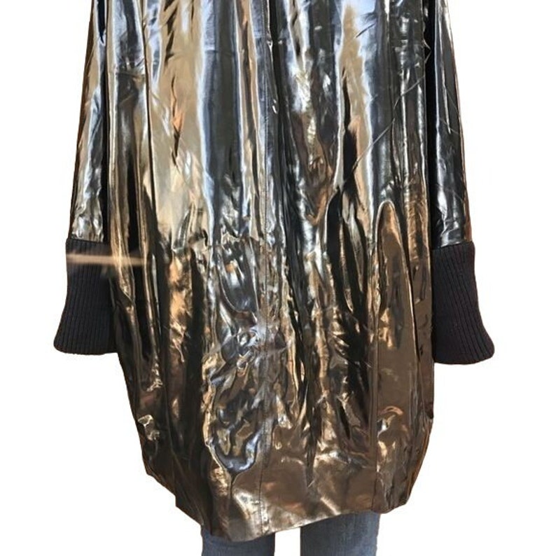 May include: A silver metallic raincoat with black ribbed cuffs. The raincoat has a shiny, reflective surface.