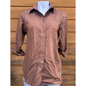 May include: A brown long-sleeved button-down shirt with a single pocket on the left chest.