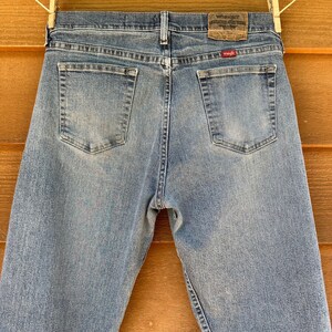 May include: A pair of light blue denim jeans with a Wrangler label on the back pocket. The jeans have a faded look and are made of a soft, comfortable material.