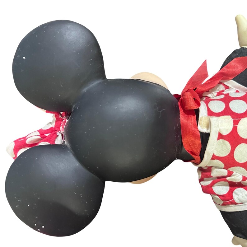 May include: A black Minnie Mouse figurine with large ears and a red and white polka dot dress. A red bow is tied around the waist. The figurine has a cream-colored face and hands.