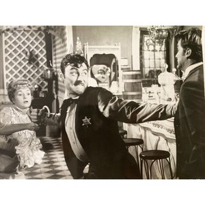 Puede incluir: Una fotografía en blanco y negro de una escena de una película. Un hombre con traje y una estrella de sheriff está tendiéndole la mano a otro hombre con traje. Una mujer con vestido está de pie detrás del sheriff, con aspecto preocupado.