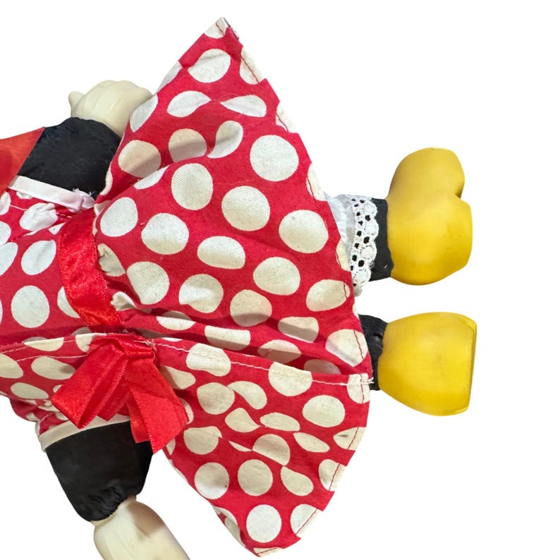 May include: A vintage doll with a red and white polka dot dress and a red bow. The doll has black sleeves, white lace trim, and yellow hands and feet. The doll's face is a pale color.