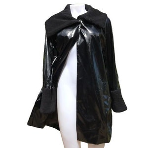 May include: A black, long-sleeved jacket with a shiny, wet-look finish. The jacket has a large, folded collar and a single-breasted closure. The sleeves have black knit cuffs.