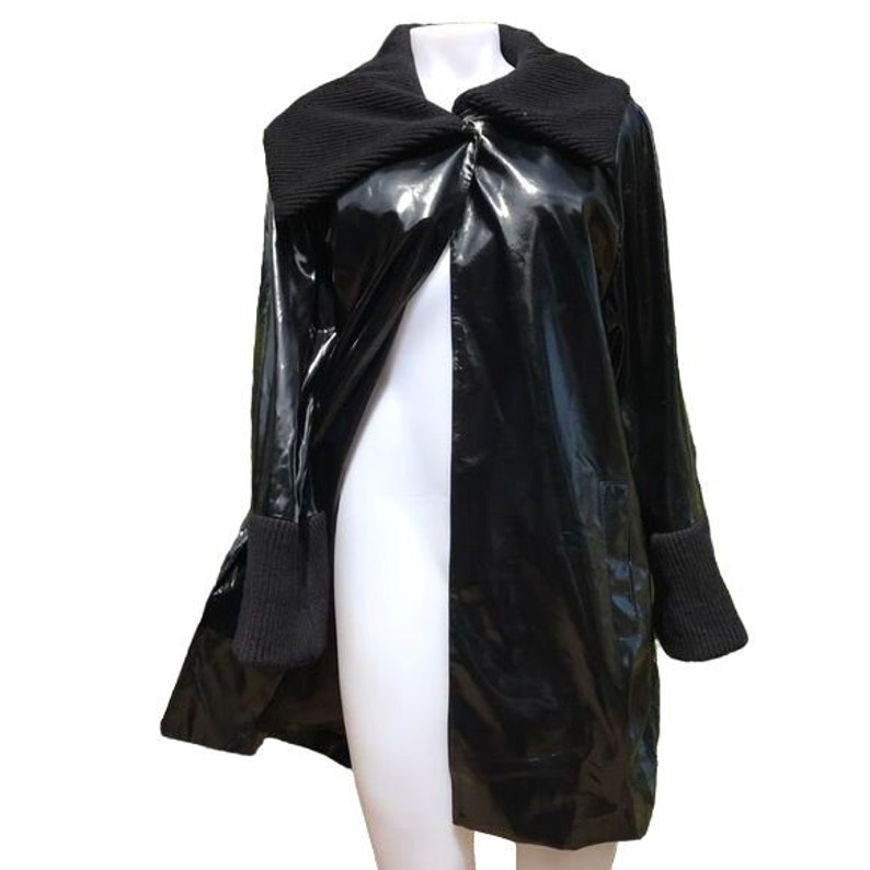 May include: A black, long-sleeved jacket with a shiny, wet-look finish. The jacket has a large, folded collar and a single-breasted closure. The sleeves have black knit cuffs.
