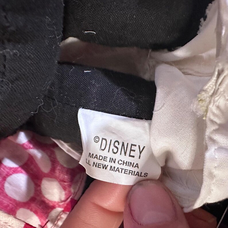 May include: Close-up of a Disney tag. The tag is white with black text that reads "&copy;DISNEY MADE IN CHINA ALL NEW MATERIALS". The tag is attached to a black fabric.