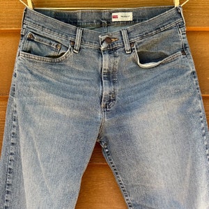 May include: A pair of light blue denim jeans with a relaxed fit. The jeans have a button fly and five pockets. The label on the waistband reads "RELAXED FIT".