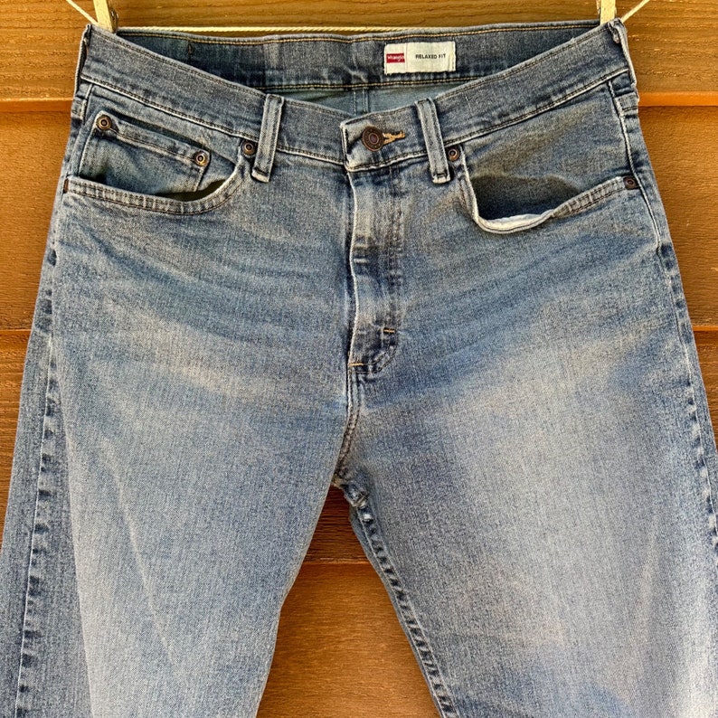 May include: A pair of light blue denim jeans with a relaxed fit. The jeans have a button fly and five pockets. The label on the waistband reads "RELAXED FIT".