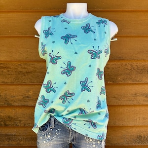 May include: A sleeveless, light blue tank top with a tie-dye effect and a pattern of green and blue butterflies.
