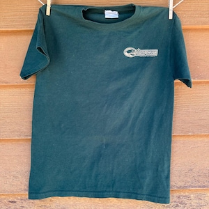 Könnte beinhalten: Ein dunkelgrünes T-Shirt mit einem weißen Logo, auf dem "Rodeo Canyon Surf Shop" mit einer Wellengrafik steht.