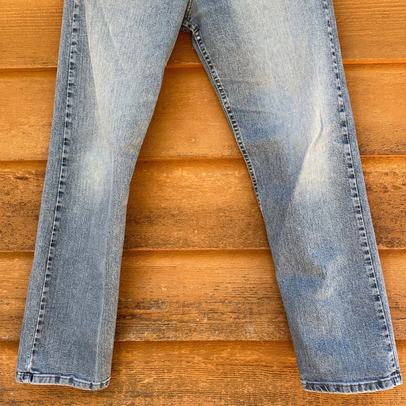 May include: A pair of light blue denim jeans hanging on a wooden surface.