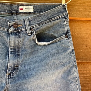 May include: A pair of light blue denim jeans with a relaxed fit. The jeans have a front pocket and a label that reads "Wrangler Relaxed Fit".