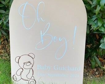 May include: A white arch-shaped sign with the text "Oh Boy!" in blue script. Below the text is a line drawing of a teddy bear and the text "Baby Guichard Due September 2024".
