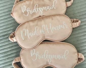 May include: Three pink satin sleep masks with white text. The top mask says "Bridemaid", the middle mask says "Maid of Honour", and the bottom mask says "Bridemaid".
