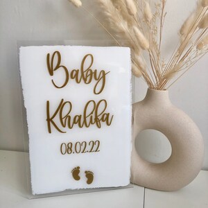 May include: A white acrylic sign with gold lettering that reads "Baby Khalifa 08.02.22" with two gold footprints below the text.