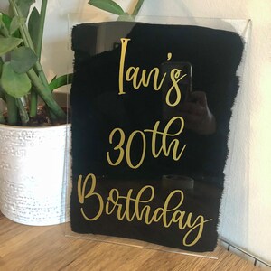 May include: A black acrylic sign with gold lettering that reads "Ian's 30th Birthday".