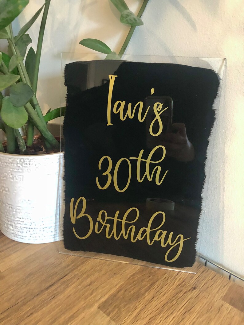 May include: A black acrylic sign with gold lettering that reads "Ian's 30th Birthday".