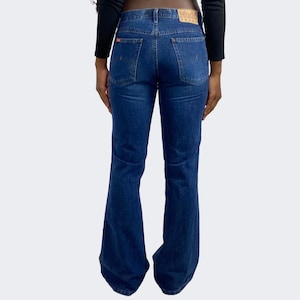 May include: A pair of dark blue denim jeans with a wide leg flare. The jeans have a classic five-pocket style and a brown leather patch on the back waistband.