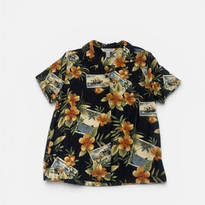 May include: A short-sleeve button-down shirt with a black background featuring a repeating pattern of orange hibiscus flowers, green tropical leaves, and rectangular framed illustrations of boats on the water. The shirt has a notched collar.