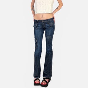 May include: Dark wash denim jeans with cargo pockets and a flared leg. The jeans have a low-rise waist and are worn with black platform sandals.