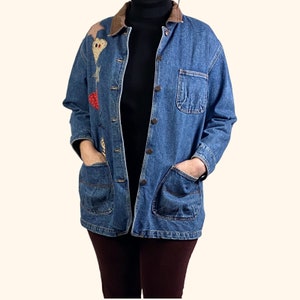 May include: A blue denim jacket with a brown corduroy collar and patchwork detailing on the left side. The jacket has two large pockets on the front and a button closure.