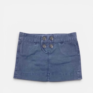 May include: A denim blue mini skirt with four decorative buttons at the waist. The skirt has a classic five-pocket design and a straight hemline. The fabric appears to be a medium-weight cotton or cotton blend.