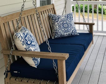 May include: A wooden porch swing with blue cushions and white and blue patterned pillows. The swing is hanging from chains and is on a wooden porch.