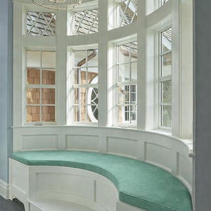 May include: A curved window seat with a light green cushion. The seat is built into a white panelled structure beneath a series of large, multi-paned windows. The windows have decorative geometric patterns at the top.