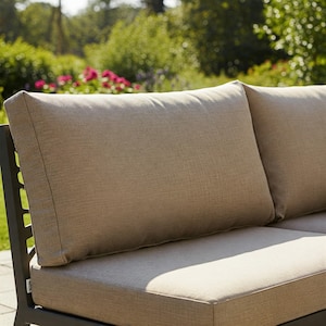 Peut inclure: Canapé d'extérieur sectionnel avec deux grands coussins rectangulaires et un coussin d'assise beige neutre. Les coussins ont un aspect texturé. Le cadre du canapé est gris foncé. L'arrière-plan présente de la verdure et des fleurs.