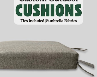 May include: A gray outdoor cushion with ties. The cushion is made of Sunbrella fabric. The text "Custom Outdoor CUSHIONS Ties Included | Sunbrella Fabrics" is printed on a white label.