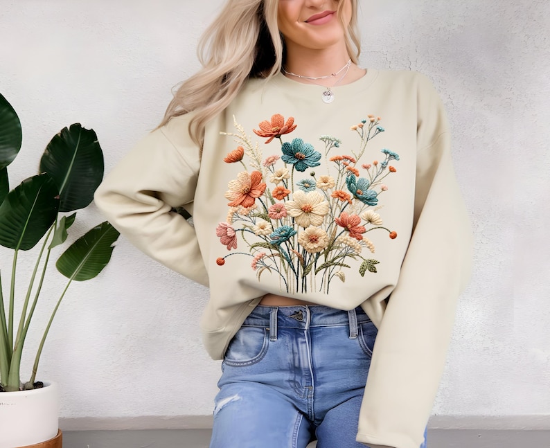 Pode incluir: Camisola bege com um design floral colorido. As flores s&atilde;o em tons de laranja, verde-azulado, rosa e creme, criando um visual vibrante e art&iacute;stico. A camisola &eacute; um estilo casual e confort&aacute;vel.