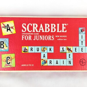 Pode incluir: Uma caixa de jogo de palavras cruzadas Scrabble para Juniores vintage. A caixa vermelha apresenta o título do jogo e ilustrações de letras e palavras. A caixa diz "New Words edition two" e "Ages 6 to 12".