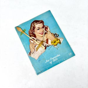Könnte beinhalten: Ein Vintage-Programm in Blau und Weiß für die Ice Capades von 1952. Das Programm zeigt ein Foto einer Frau in einem weißen Eiskunstlaufkostüm, die ein Paar Schlittschuhe hält. Der Text "Ice Capades von 1952" ist in Schwarz auf dem Programm gedruckt. Der Preis beträgt 50 Cent.