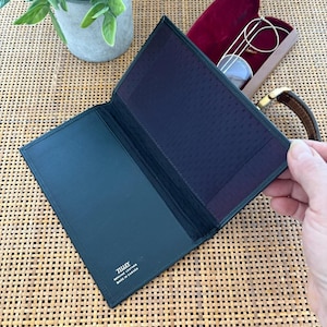 Puede incluir: Una cartera de cuero negro con una superficie texturizada. La cartera está abierta y el interior está forrado con una tela de color morado oscuro. La cartera tiene el texto "TULUX GENUINE LEATHER MADE IN CANADA" impreso en el interior.