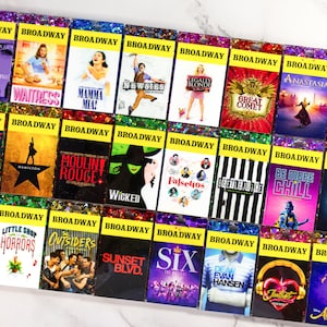 Peut inclure: Une collection de 24 porte-clés en résine carrés, colorés et scintillants, représentant des titres et logos de spectacles de Broadway. Les porte-clés sont disposés en quatre rangées de six. Les porte-clés sont tous de couleurs différentes et présentent une variété de motifs. Parmi les spectacles représentés, on trouve "Hadestown", "Waitress", "Mamma Mia!" et "Wicked".