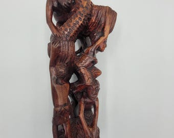 May include: A hand-carved wooden sculpture of three figures intertwined, with intricate details and a dark brown finish.