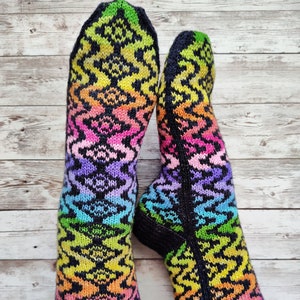 May include: A pair of colorful knitted socks with a rainbow pattern. The socks are black with a green, yellow, orange, pink, blue, and purple pattern.