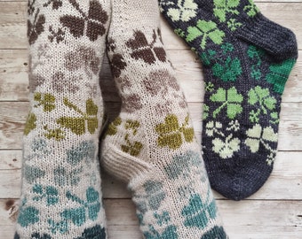 May include: Knit socks with a clover pattern in shades of beige, brown, green, and teal. One pair is on a person's feet, and another pair is displayed separately. The socks are made of a soft, textured yarn.