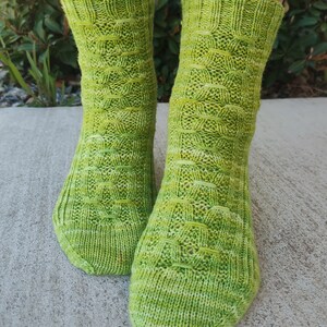 Puede incluir: Un par de calcetines de punto verde y blanco con un patrón texturizado. Los calcetines están hechos con un hilo jaspeado que crea un sutil efecto degradado.