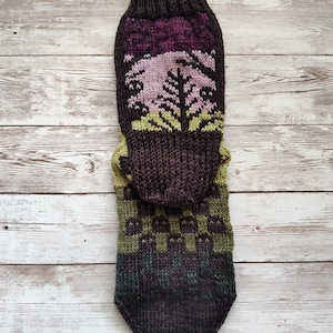 May include: A pair of knitted socks with a brown, green, and purple color scheme. The socks feature a forest scene with trees and a sunset.