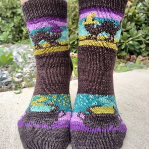 Puede incluir: Un par de calcetines de punto marrón con rayas de colores y un patrón de animales. Los calcetines tienen una raya morada, azul verdoso y amarilla con un diseño de animal marrón.