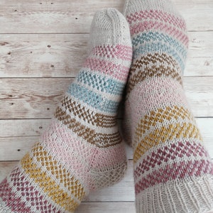May include: A pair of knitted socks with a striped pattern in shades of pink, brown, yellow, and blue. The socks are made with a soft, textured yarn.
