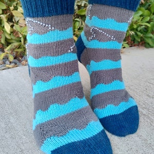 Puede incluir: Un par de calcetines de punto a rayas azules, grises y turquesa con un diseño de cuentas. Los calcetines son de tobillo y tienen un puño acanalado.