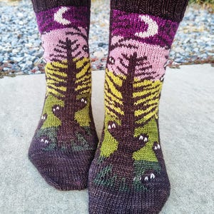 May include: A pair of brown, pink, green, and yellow knitted socks with a moon and tree design. The socks have a whimsical pattern of owls with white eyes.