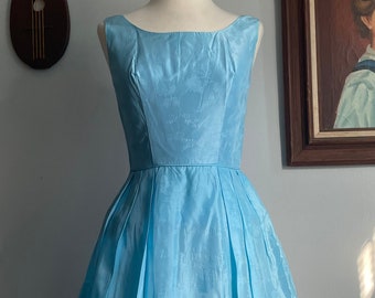 May include: A light blue sleeveless dress with a full skirt. The dress is on a mannequin in front of a white wall.