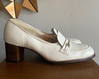Puede incluir: Zapatos de vestir blancos de cuero con tacón, hebilla dorada y tacón de madera.