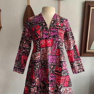 May include: A pink and black patterned dress with a V-neck and long sleeves. The dress has a geometric pattern with a Polynesian-inspired design.