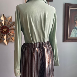 May include: A light green long-sleeved shirt with a collared neckline and brown and white striped trousers.
